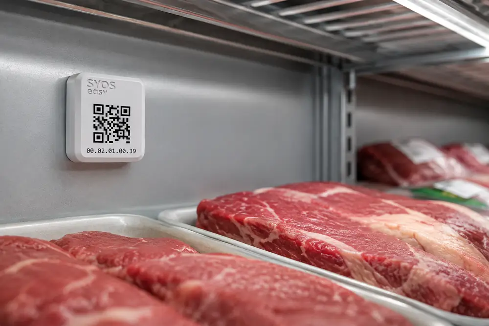 Celular com o app SyOS aberto, com balcão de carnes refrigerado ao fundo